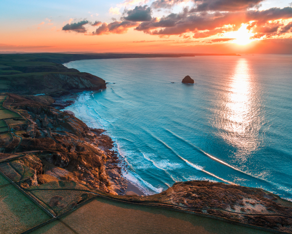 A silhouetted lighthouse on a cliff edge at sunrise 