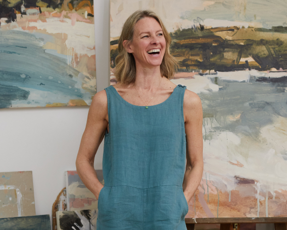 A woman in a blue top laughing in front of abstract landscape paintings