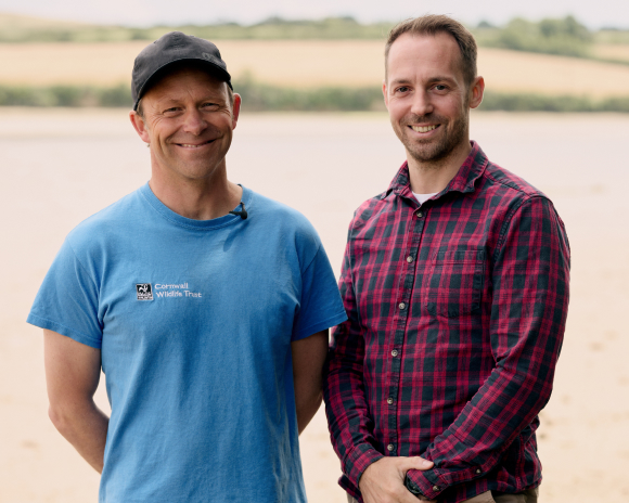 Two men one in a blue top and cap and one in a burgundy checked shirt smiling at the camera