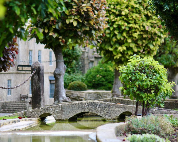 Grey bridge over river with green trees in the foreground and background